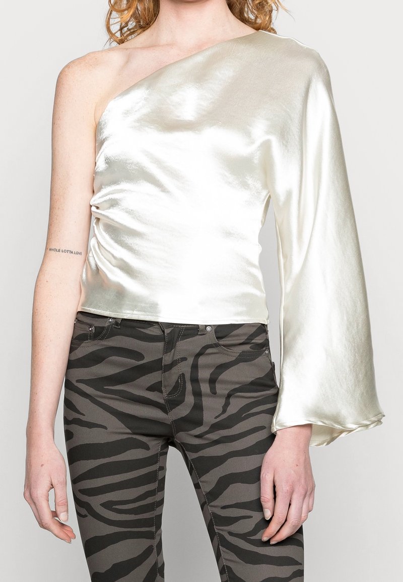 Top na jedno rameno ve lesklém slonovinovém saténu, zdobený detailním řasením a kalhotovým rukávem. V páru s olivově zelenými džínami s pruhy zebry.