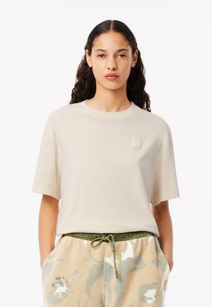 Lichtbeige katoenen t-shirt met korte mouwen, ronde hals en een getextureerd vierkant logo op de borst. Eenvoudig, minimalistisch ontwerp.