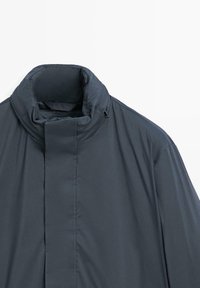 Dunkelgraue Jacke mit hohem Kragen und Frontverschluss. Der Stoff ist glatt und verfügt über Nahtdetails sowie ein insgesamt minimalistisches Design.