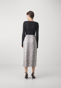 Black long-sleeve top paired with a knee-length skirt featuring a grey and white snake print. The outfit is completed with black high-heeled shoes.
