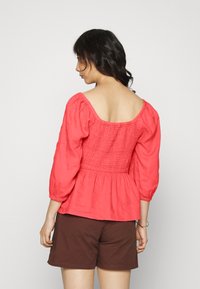 Top peplum em mistura de linho coral, com mangas de três quartos, costas franzidas e decote quadrado, combinado com calções castanhos.