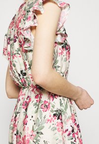 Kukallinen mekko kevyestä kankaasta, jossa on röyhelöhihoja, vaalea tausta, vaaleanpunaisia ja vihreitä kukkakuoseja, rypytetty vyötärö ja sivuprofiili.