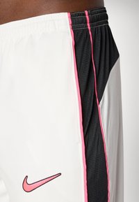Shorts de sport Nike avec un corps blanc et des panneaux en maille noire, des accents roses et un logo. Taille élastique et rayures latérales distinctes.