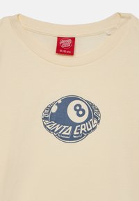 Krämfärgad bomullströja med en blå grafik av en biljardboll med texten "Santa Cruz", rund halsringning och korta ärmar.