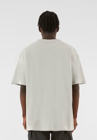 Lys grå overdimensjonert t-skjorte, rund hals, korte ermer, laget av myk bomull. Minimalistisk design uten synlige logoer eller detaljer.
