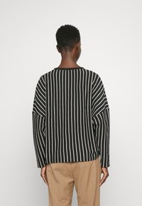 Suéter a rayas en blanco y negro con un tejido texturizado, ajuste relajado y hombros caídos, combinado con pantalones beige.
