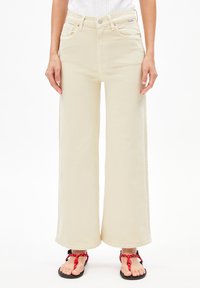 Beige wijde jeans van denim, met een hoge taille, voorzakken en opgerolde hemden, gecombineerd met zwarte sandalen met rode accenten.