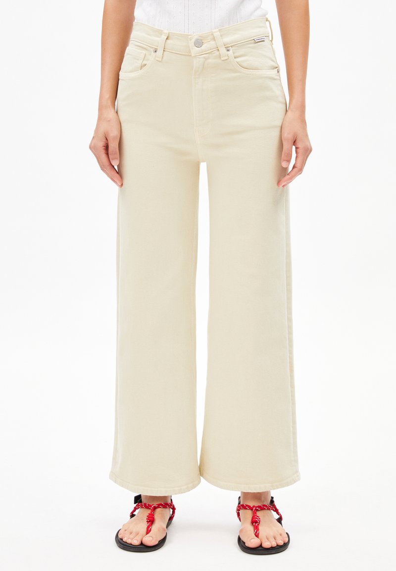 Beige wijde jeans van denim, met een hoge taille, voorzakken en opgerolde hemden, gecombineerd met zwarte sandalen met rode accenten.