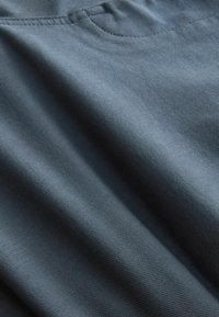 Sötétszürke, sima tapintású szövet finom vízszintes csíkokkal; a felső szél közelében egy kis zseb található.