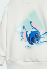 Biała bluz sweatshirtowa z niebieską postacią z różowymi akcentami. Ilustracja postaci znajduje się na środku przodu na tle o teksturowanej fakturze.