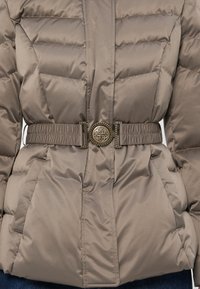 Jachetă de culoare taupe, căptușită, cu cusături matlasate, curea elasticizată cu o cataramă rotundă aurie cu inițiale intercalate gravate.