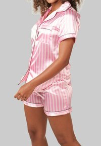 Ensemble de pyjama en satin rayé rose avec un haut à manches courtes, une poche et un short assorti avec des accents en passepoil noir. Texture lisse.
