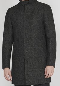Czarny i szary płaszcz w jodełkę z wysokim kołnierzem, zapięciem na jeden guzik i bocznymi kieszeniami; tkana tekstura nadaje głębi projektowi.