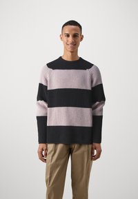 Pulover din tricot cu model rib ce are dungi mari orizontale în gri închis și roz deschis, având un guler rotund și o croială lejeră.