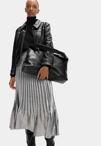 Zwarte leren jack met studs op de kraag, strakke zwarte coltrui, metallic zilveren geplooide rok en een zwarte oversized handtas.