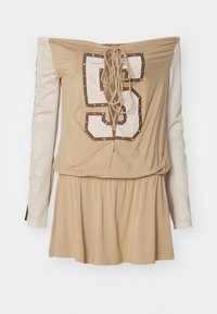 Beżowa sukienka typu off-shoulder z lace-up z tyłu, z długim rękawem z białej siateczki i dużą nadrukowaną cyfrą "5" ozdobioną ćwiekami.