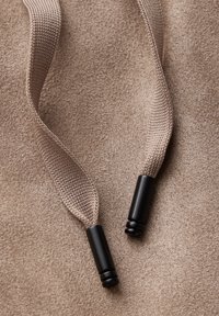Två ljusbruna dragsnoddar med svarta metallspetsar på en texturerad beige yta, som visar ett mjukt och smidigt material.