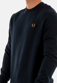 Sudadera azul marino hecha de una suave mezcla de algodón, con cuello de tripa y puños acanalados. Pequeño logo dorado de laurel en el lado izquierdo del pecho.