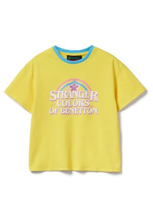 T-shirt gialla a maniche corte con colletto blu, testo frontale "Stranger Colors of Benetton" e un arcobaleno pastello con stelle e cuori sopra il testo.