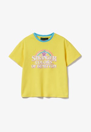 Geel T-shirt met korte mouwen en blauwe kraag, voorzijde met de tekst "Stranger Colors of Benetton" en een pastelregenboog met sterren en harten boven de tekst.