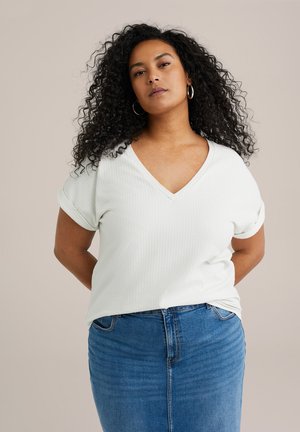 White, textured V-neck t-shirt with rolled sleeves, paired with a blue denim skirt. The fabric has a subtle pattern, enhancing visual interest.