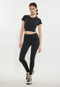 Sort aktivtøjssæt med en cropped top og højtaljede leggings, lavet af glat, strækbart stof, der har slanke linjer og minimale sømme.