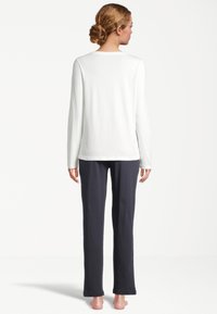 Witte lange mouwtop met een ronde hals, gecombineerd met navyblauwe, loszittende broek, beide gemaakt van zachte, comfortabele stof.