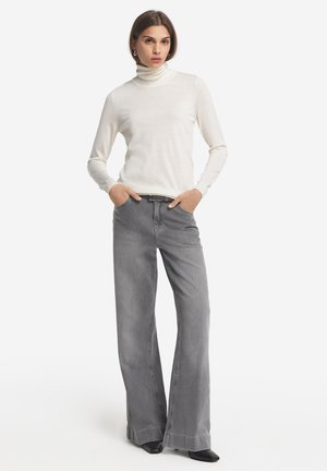 Jean gris évasés associés à un col roulé blanc ajusté. La tenue présente une texture lisse et des détails matériels minimalistes.