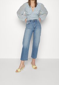 Ljusblå blommig blus med voluminösa genomskinliga ärmar, ihop med högmidjade raka denimjeans och gula klacksandaler.