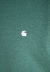 Green knit fabric provides a smooth texture, featuring a small white logo on the right side. The design is simple and uniform.