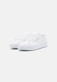 Zapatillas de cuero blancas con textura suave, punta redondeada, cordones en la parte frontal y un sutil logo en el costado. Suela de goma plana.