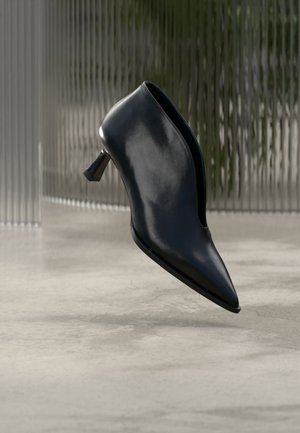 Bottine noire en cuir à bout pointu, design ajusté et talon de hauteur moyenne à forme unique sur un sol en béton lisse.