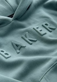 Kapucnis pulóver tompa türkizkék színben, megemelt "BAKER" felirattal. Puha szövet textúrával és kényelmes kapucnival rendelkezik. Minimalista kialakítás, minták vagy díszítések nélkül.