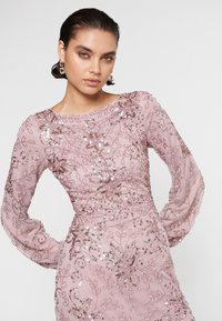 Vestido rosa de manga larga con embellishments de lentejuelas florales, escote barco y tejido texturizado para una silueta ajustada.