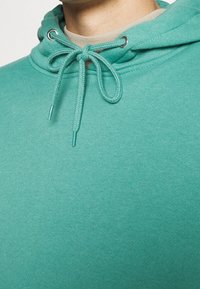 Felpa turchese con cappuccio, dotata di un cordino con aglette argentate, realizzata in un tessuto morbido con una superficie liscia e una vestibilità comoda.