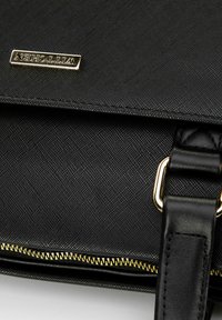 Schwarze, strukturierte Handtasche mit einer goldenen Logo-Plakette, Reißverschlüssen mit goldenen Akzenten und einem Ledertragegurt mit rechteckiger Metallöse.