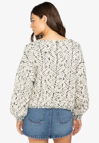 Crème trui met een geometrisch zwart patroon, oversized pasvorm, geribbelde manchetten en onderrand. Gecombineerd met een dennenrok.