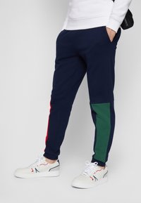 Tumed joggers punaste ja roheliste külgpanelidega, millel on elastne vöökoht ja kaks külge taskut. Kombineeritud valgete spordijalatsitega.