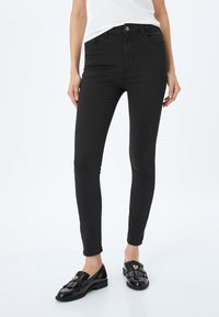Svarta, smala jeans i en elastisk bomullsblandning. Har knäppning fram, fickor och en slät, matta yta.