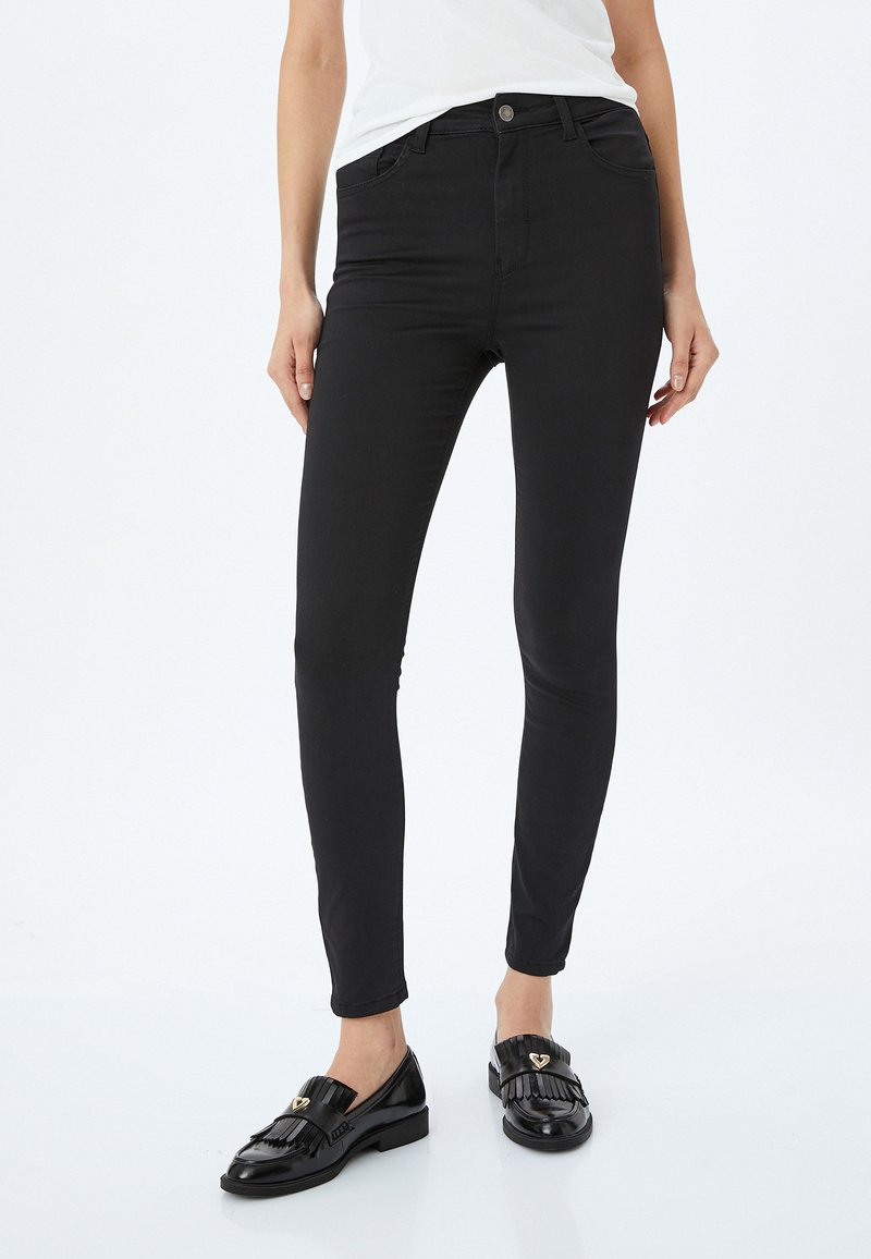 Svarta, smala jeans i en elastisk bomullsblandning. Har knäppning fram, fickor och en slät, matta yta.