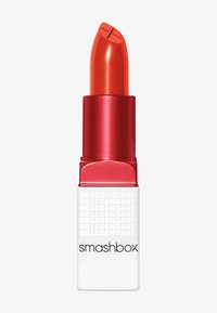 Un lápiz labial rojo en un elegante tubo metálico rojo con una base blanca cuadrada. Presenta el logo "smashbox" y el texto "BE LEGENDARY" en un patrón repetido.