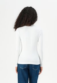 Weißes Langarmhemd aus glattem Stoff, figurbetontes Design und schmale Manschetten, kombiniert mit blauen Denim-Jeans.