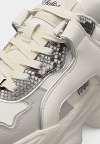 Baskets blanches épaisses avec texture en peau de serpent, lacets épais et étiquette de marque Buffalo sur le côté.