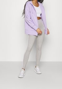 Ljuslila zip-up hoodie, grå leggings med vita sidostråk och vita sneakers. Materialet verkar mjukt och töjbart.