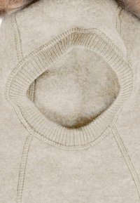 Beżowy wełniany ubiór z okrągłym wycięciem przy szyi, z prążkowanym kołnierzem i gładką fakturą, podkreślający miękki materiał.