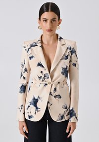 Bloemige blazer in crèmewit met marineblauwe aquarelpatronen, enkele knoopsluiting, getailleerde snit en lange mouwen. Gecombineerd met donkerdenim.