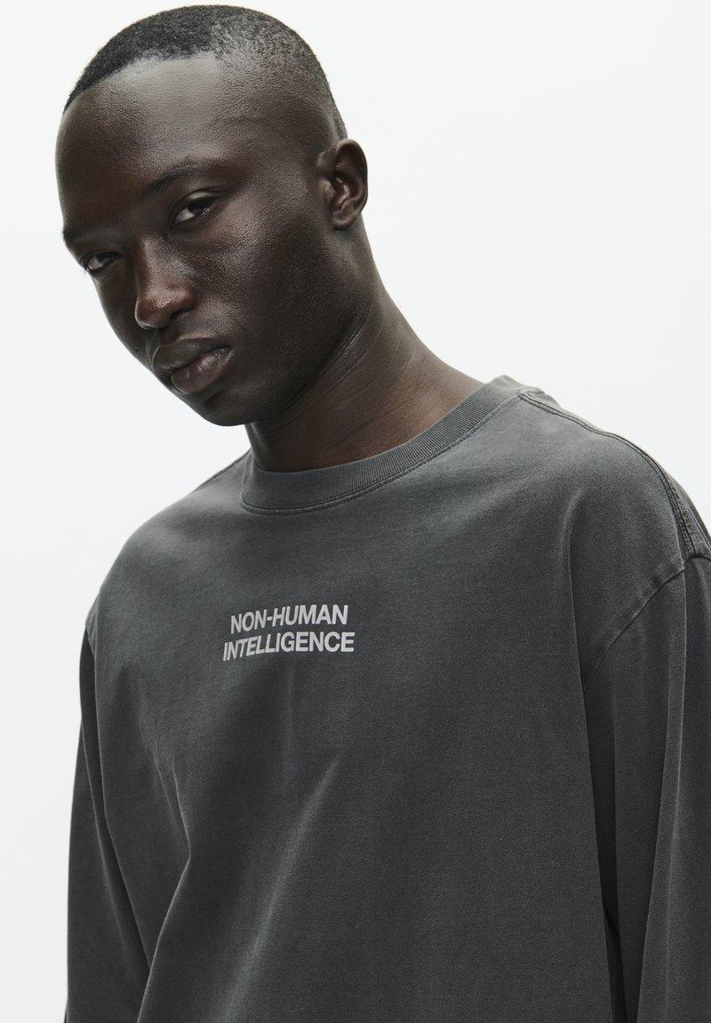 T-shirt à manches longues gris foncé en coton, avec le texte "INTELLIGENCE NON-HUMAINE" en blanc, de coupe décontractée et avec un col rond.