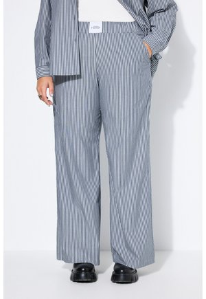 Persona que lleva pantalones sueltos de cintura alta con rayas verticales azules y blancas combinados con una camisa abotonada a juego y zapatos negros gruesos.