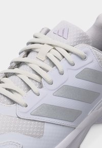 Κοντινό πλάνο λευκού αθλητικού παπουτσιού Adidas με ύφασμα πλέγματος, κορδόνια δεμένα και τρεις ασημένιες ρίγες στην πλευρική επιφάνεια.