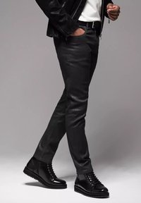 Pantalones de cuero negro con corte ajustado y bolsillos con cremallera, combinados con botas de tobillo negras de cordones con un acabado suave y suela texturizada.